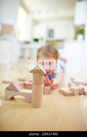 Child builds a house with wooden building blocks on the floor Stock Photo