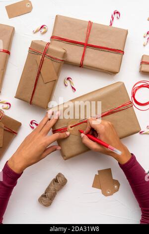 Female's hands writing Christmas cards on gift boxes decorated with kraft paper Stock Photo