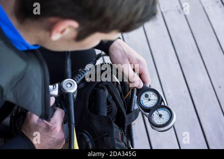 Scuba diver kitting up and checking the pressure gauge, close up of hand holding equipment over shoulder shot. Stock Photo