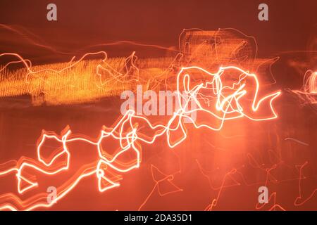 Long exposure light painting photography, curvy lines of vibrant neon metallic red-orange colors against a black background. Stock Photo