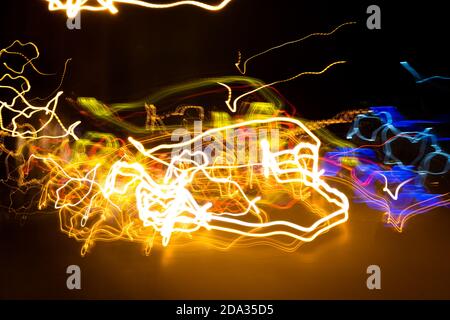 Long exposure light painting photography, curvy lines of vibrant neon metallic yellow blue colors against a black background. Stock Photo