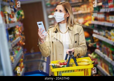 Adult woman in medical mask using smartphone and shopping for groceries Stock Photo