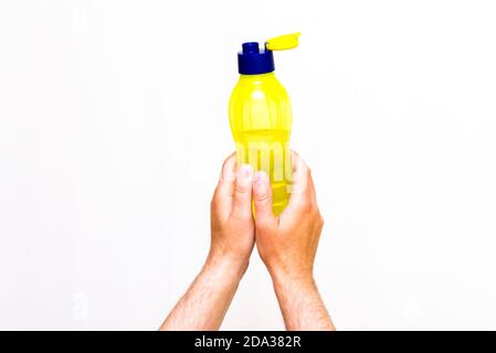 Man's hands holds yellow bottle of water, isolated on white studio background. Close up image. Stock Photo