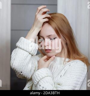 portrait of a sad beautiful 16 year old caucasian girl in a white knitted sweater Stock Photo