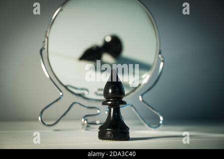 A chess piece is reflected in the mirror. Things and people are not what they seem. Reassessment of their abilities. Psychology, motivation. Power of Stock Photo