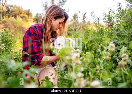 Young latin woman with her dog sitting in a flower field surrounded by tall grass Stock Photo