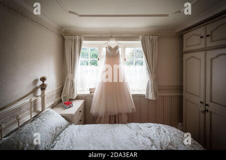 Bride's wedding dress hanging at a bedroom window. Stock Photo