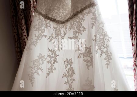 Bride's wedding dress hanging at a bedroom window. Stock Photo