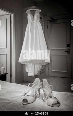 Bride's wedding dress hanging on a wardrobe with shoes in the foreground. Stock Photo