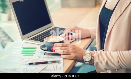Business woman hands typing on laptop while drinking coffee in modern office workplace Stock Photo