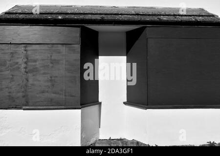 close up of bay windows boarded up with black board on an empty house painted white in sunlight Stock Photo