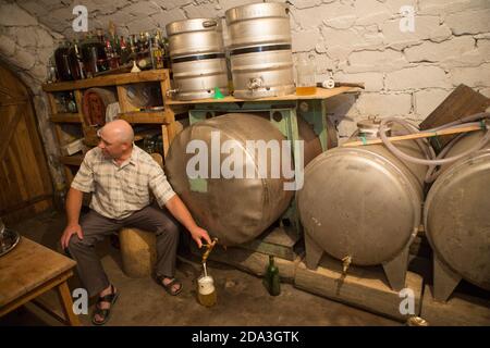 A farmer pours a pitcher of homemade wine from a vat in his cellar in Kalaraci District, Moldova. Stock Photo