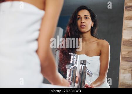 Beautiful brunette standing in bathroom near the mirror and washing hands Stock Photo