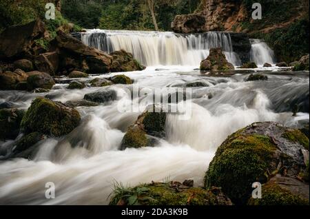 Motion blur waterfall among trees, green leaves, rocks and stones in forest with cascade river in Belarus. Stock Photo