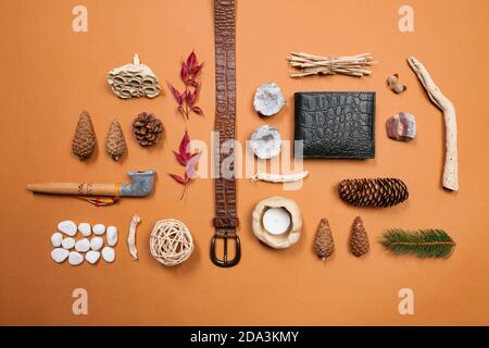 Still life composition of belt, wallet, peace pipe and natural things like pine cones, white stones, red leafs and minerals on a brown background Stock Photo