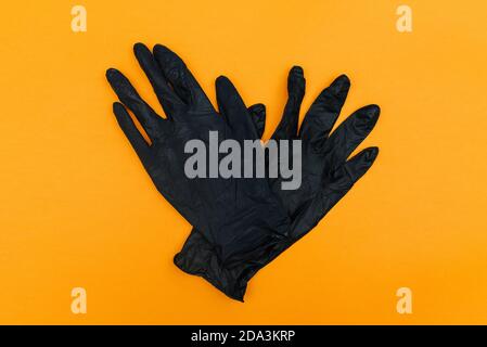 Black disposable gloves isolated on orange background. Hand protection from coronavirus, hygiene. Top view, flat lay