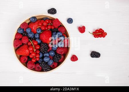 Mix of berries in bowl on white wooden background Stock Photo