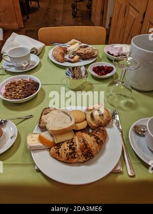 Breakfast served on a table with green tablecloth. Pastries, piece of bread, cheese, croissant, granola yogurt, jam, glasses, cups. Stock Photo