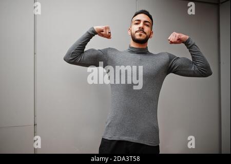 Portrait of stylish arab beard man wear grey turtleneck. Arabian model guy against steel wall shows his biceps. Stock Photo