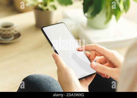 Mockup of a phone held by a woman who is touching screen in the living room. White screen Stock Photo
