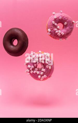 Close-up of three donuts, two roses and one chocolate, levitating on a pink background. Vertical photography Stock Photo