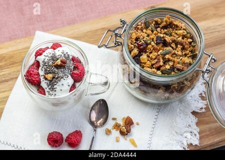 Granola in a jar and in a cup with yogurt and raspberry top view. Granola is a breakfast food and snack food consisting of rolled oats, nuts, honey, that is baked until golden brown Stock Photo