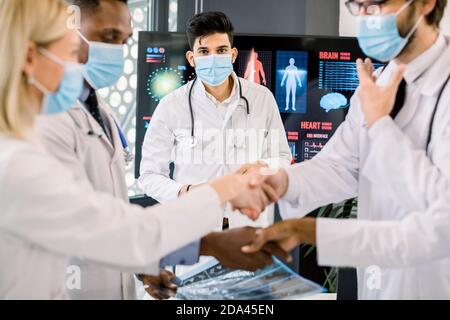 Pandemy, outbreak of coronavirus concept. Close up cropped image of multiethnic group of doctors with face masks, shaking hands on the morning staff Stock Photo