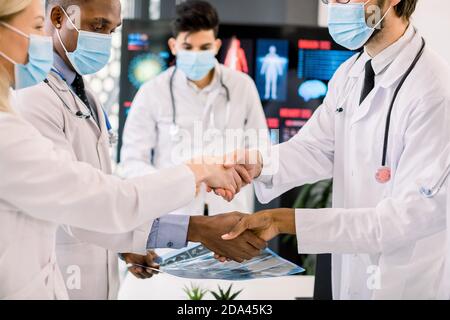 Pandemy, outbreak of coronavirus concept. Close up cropped image of multiethnic group of doctors with face masks, shaking hands at the meeting. Focus Stock Photo