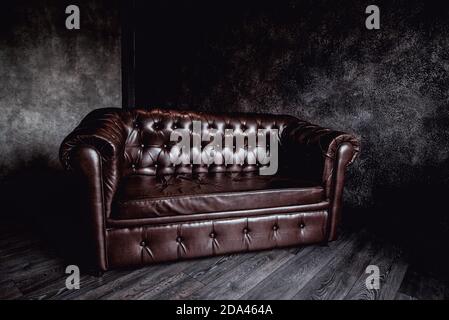 big brown leather sofa in a dark room gray walls concrete Stock Photo