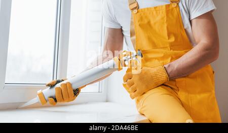 Handyman in yellow uniform works with glue for window indoors. House renovation conception Stock Photo