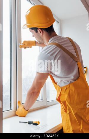 Handyman in yellow uniform installs new window. House renovation conception Stock Photo