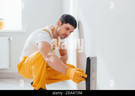 Handyman in yellow uniform polishing wall indoors. House renovation conception Stock Photo
