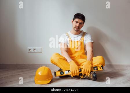 Tired handyman in yellow uniform sits indoors and takes break. House renovation conception Stock Photo