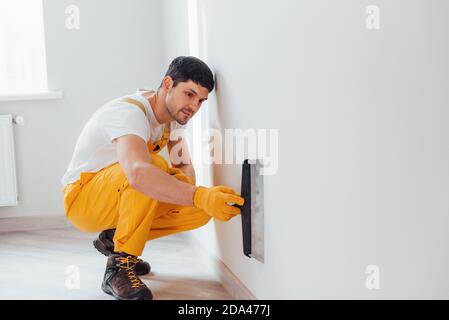Handyman in yellow uniform polishing wall indoors. House renovation conception Stock Photo