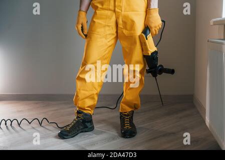 Handyman in yellow uniform with drill standing indoors. House renovation conception Stock Photo