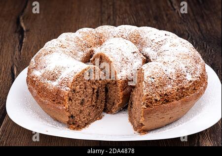 A ring-shaped cupcake sprinkled with powdered sugar. Slice in the middle of the cupcake on a white plate. Homemade cupcake. Stock Photo