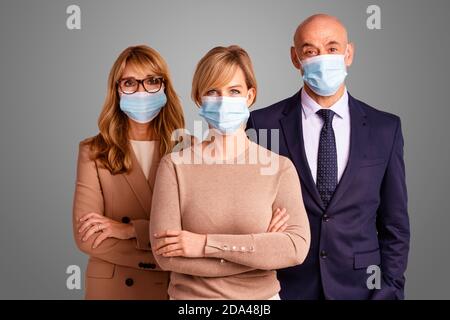 Group of business people wearing face masks and looking at camera while standing together at isolated background. Stock Photo