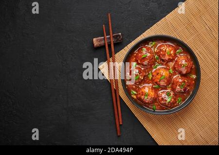 Veg Manchurian Gravy Balls in black bowl in dark slate table top. Vegetarian Manchurian is indian chinese cuisine dish. Asian food and meal. Top view. Stock Photo