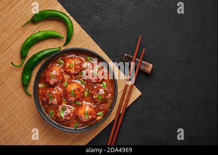 Veg Manchurian Gravy Balls in black bowl in dark slate table top. Vegetarian Manchurian is indian chinese cuisine dish. Asian food and meal. Top view. Stock Photo