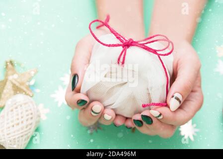 Beautiful festive female manicure. Women's hands hold a small gift. New Year's content, balls, sequins, stars. Merry christmas Stock Photo
