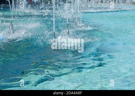 Smooth bore nozzles for foam jet water stream effect with splashes. Ripple and reflection on turquoise water surface of city fountain. Urban water fea Stock Photo