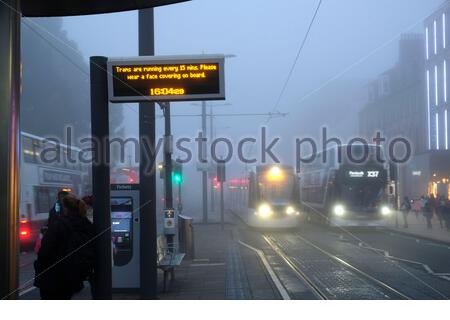 Edinburgh, Scotland, UK. 9th Nov 2020. Thick Afternoon fog persists in the city centre, trams and buses seen here in Princes Street with a tram approaching the Tramp Stop reminding passengers to wear a facemask.  Credit: Craig Brown/Alamy Live News Stock Photo