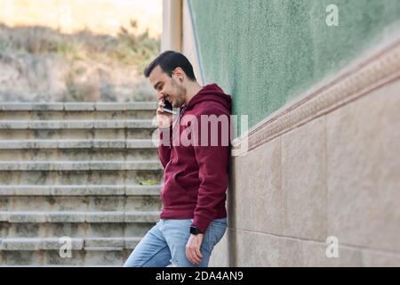 Young man talks on his phone leaning against a wall Stock Photo