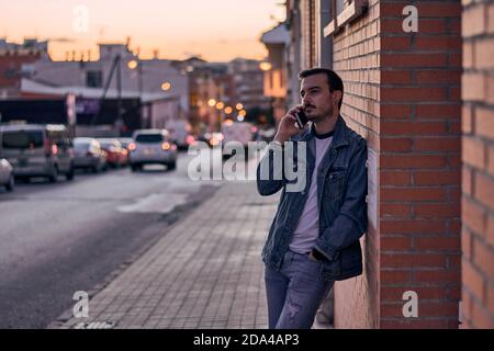 Young man talks on his phone leaning against a wall Stock Photo