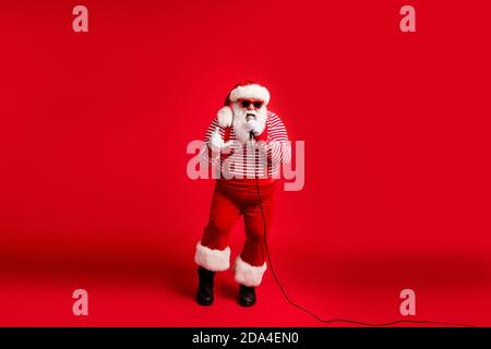 Full length body size view of his he handsome bearded fat overweight cool talented Santa vocalist rock roll star singing hit showing horn sign Stock Photo