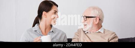 cheerful woman with cup of tea talking to happy elderly father, banner Stock Photo