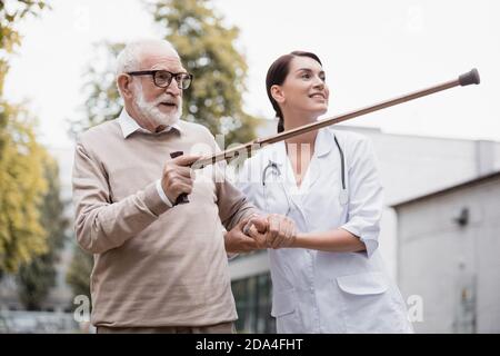 aged man pointing with walking stick away near smiling geriatric nurse Stock Photo