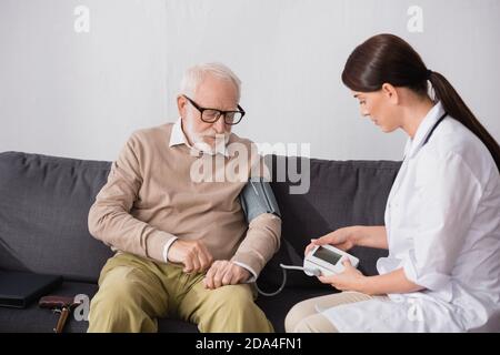 brunette geriatric nurse examining aged man with tonometer at home Stock Photo