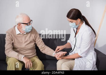 brunette nurse checking pressure of aged man with stethoscope Stock Photo
