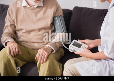 cropped view of geriatric nurse examining aged man with tonometer at home Stock Photo